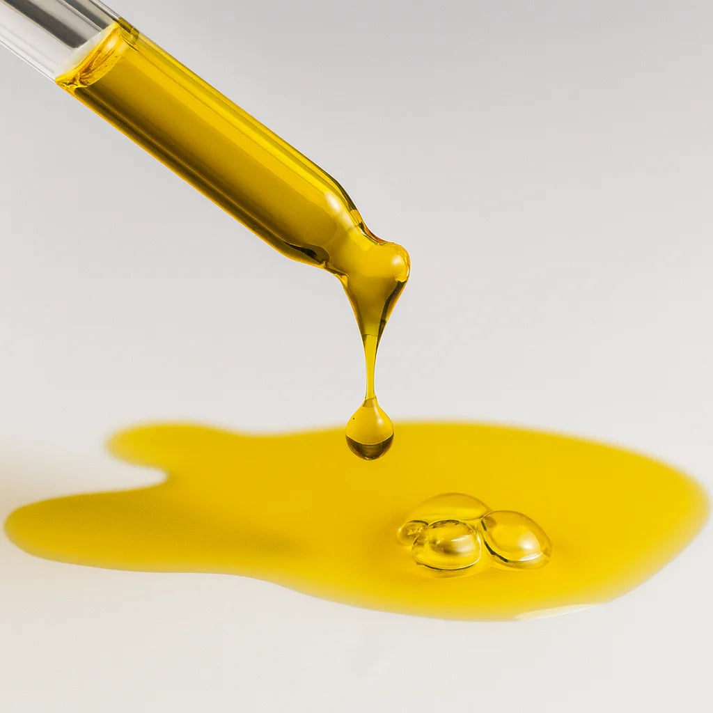 Yellow liquid being dripped from a pipette onto a white surface.