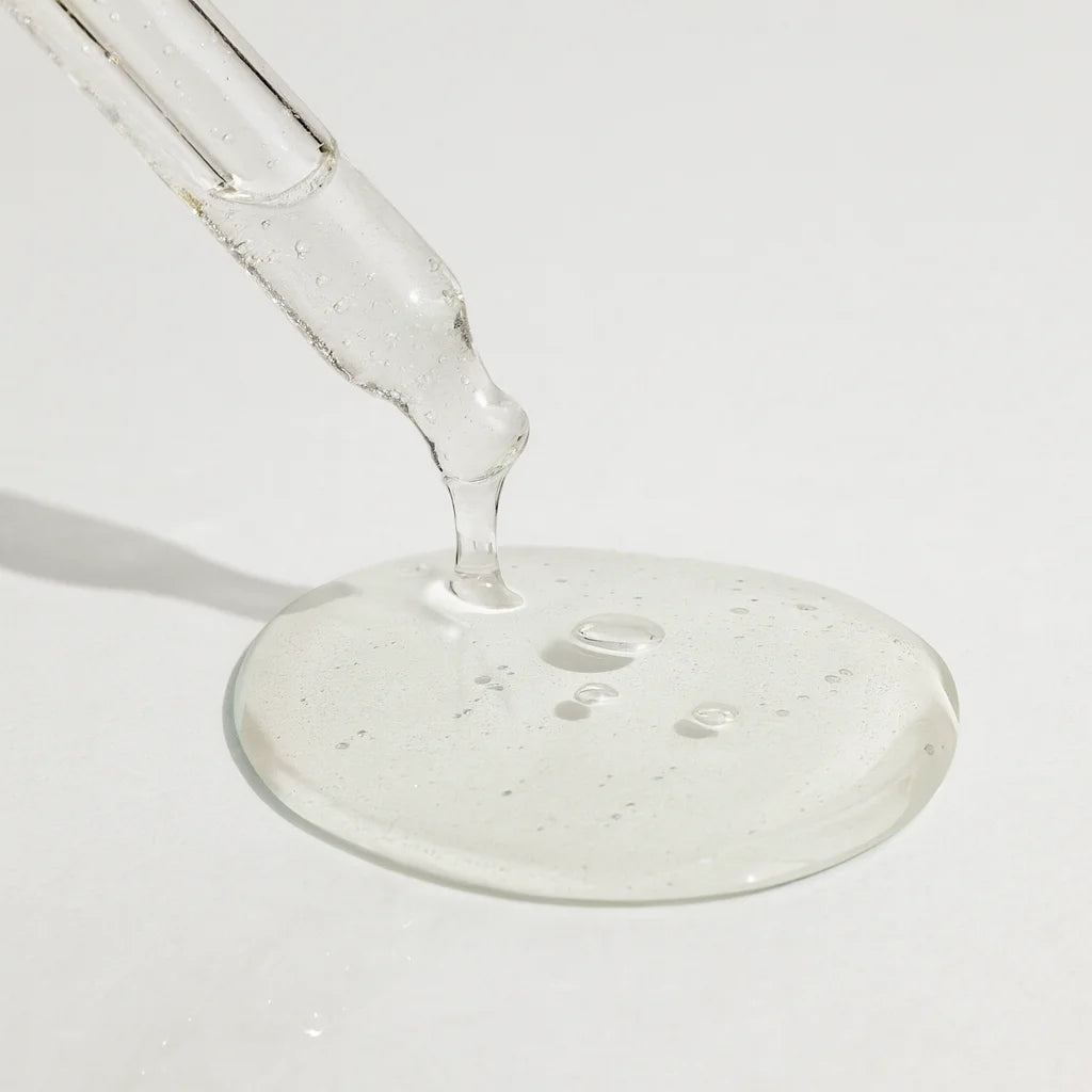 Clear liquid being poured from a glass dropper onto a white surface.