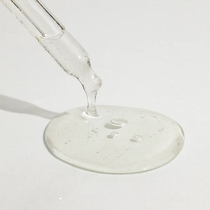 Clear liquid being poured from a glass dropper onto a white surface.