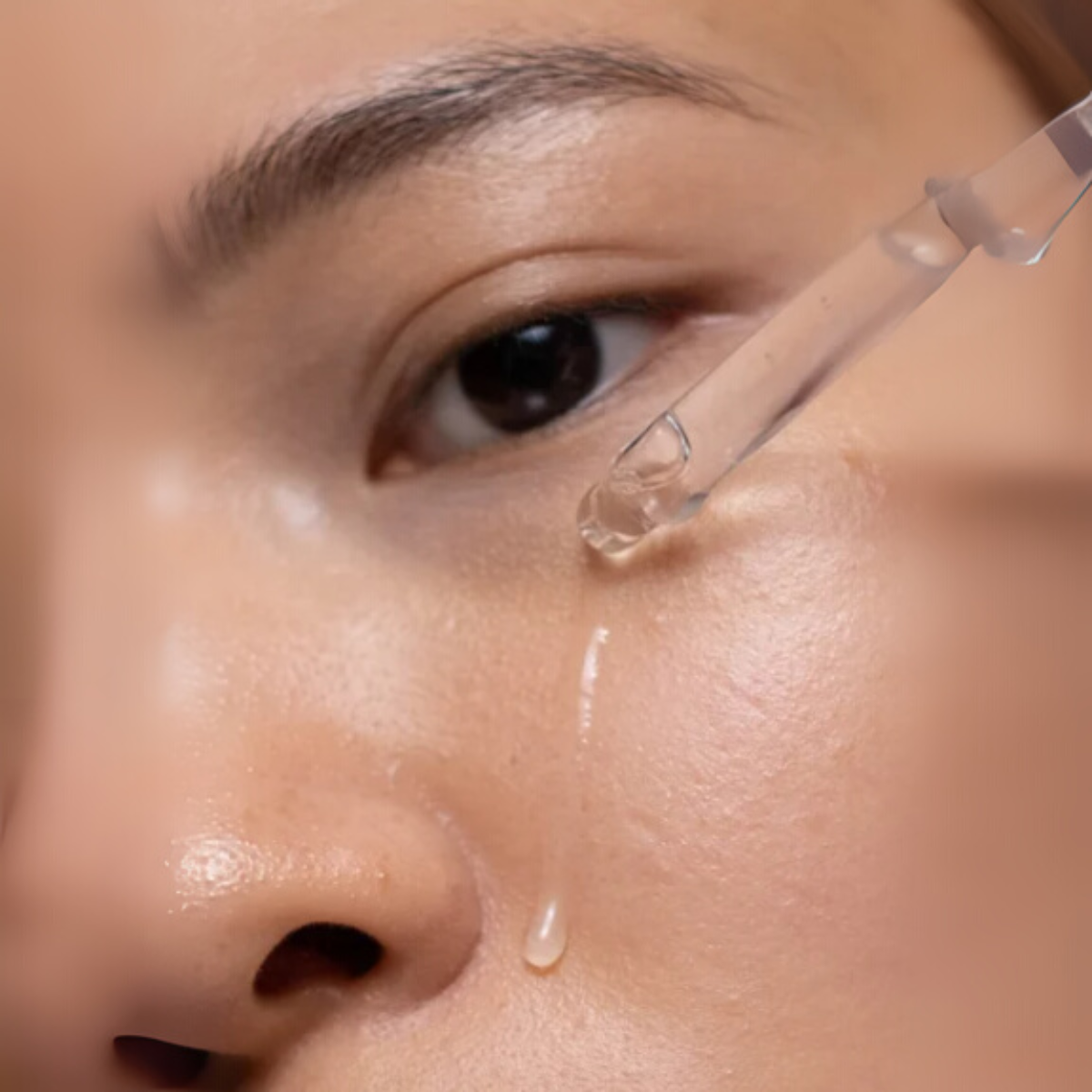 Close-up of a person applying a dropper of liquid to their skin.